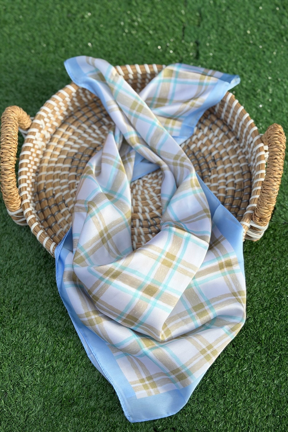 Blue plaid scarf sitting in a tan basket on a green turn backdrop.