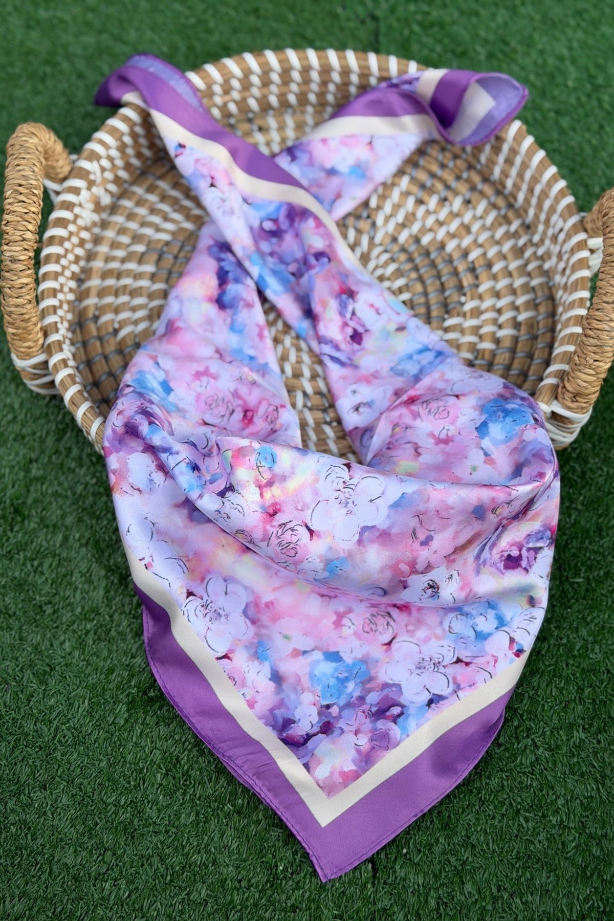lavender scarf with flower decor resting on a tan basket with a green turf background