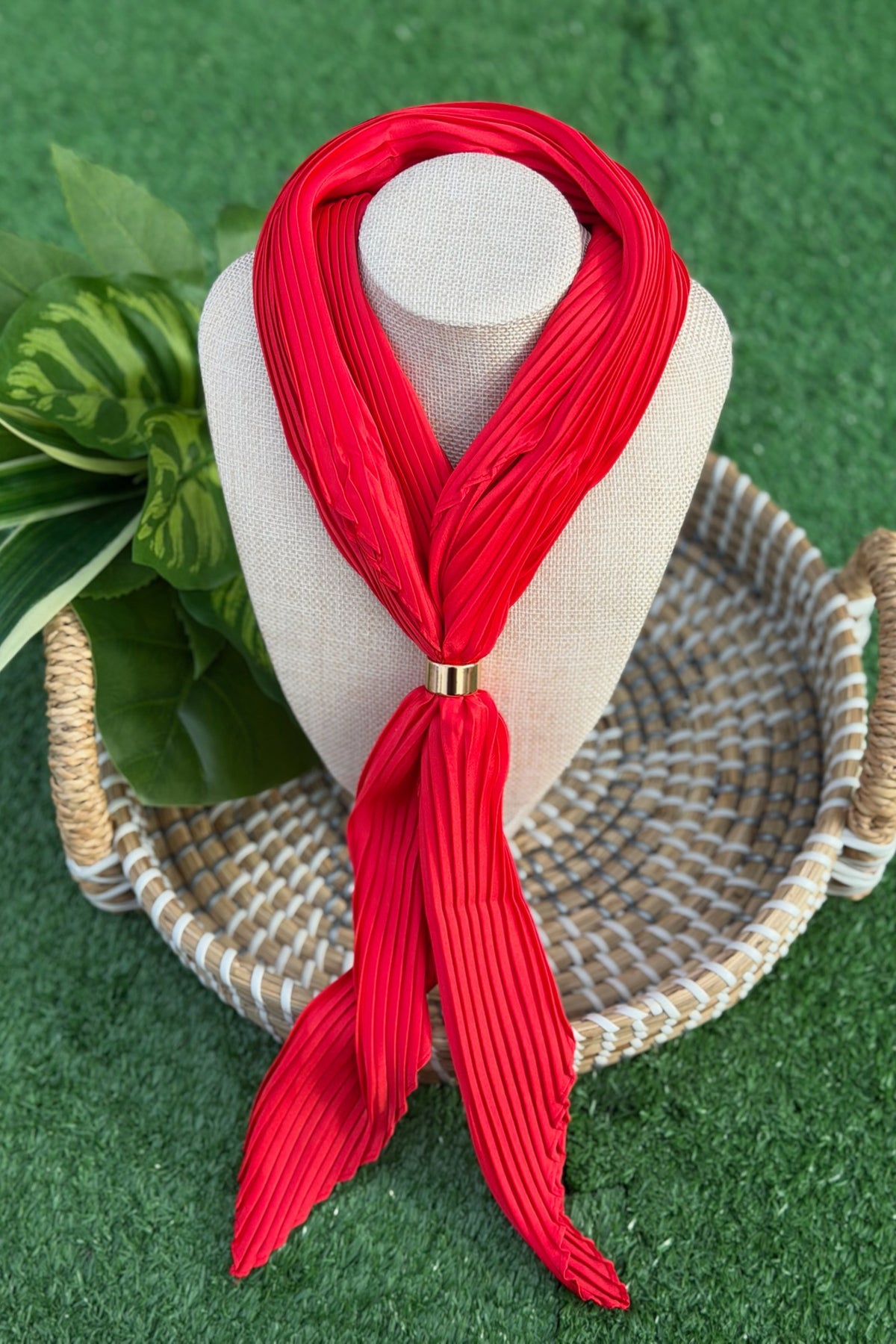 Red scarf on a mannequin head with a woven basket and plant on a green background