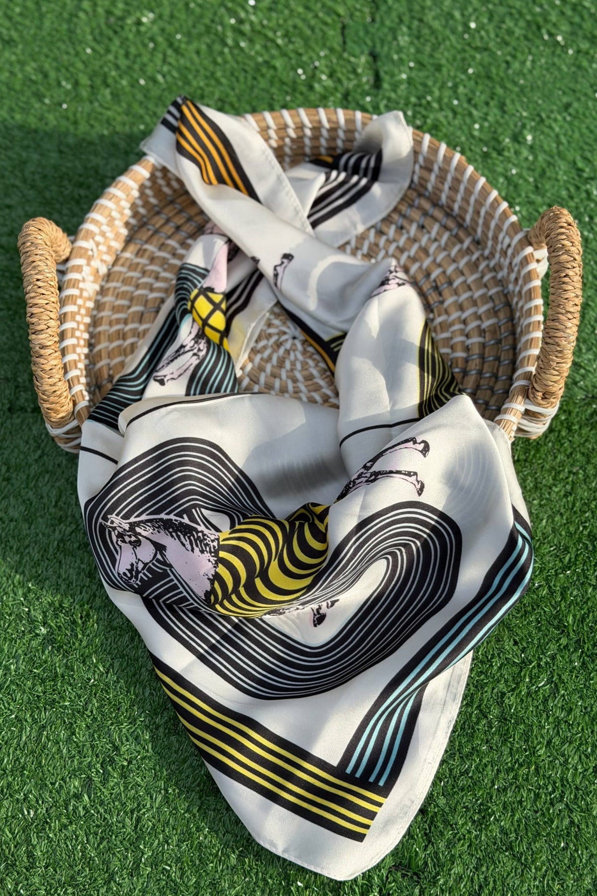grey scarf with horses on it folded over a tan basket on a turn backdrop.