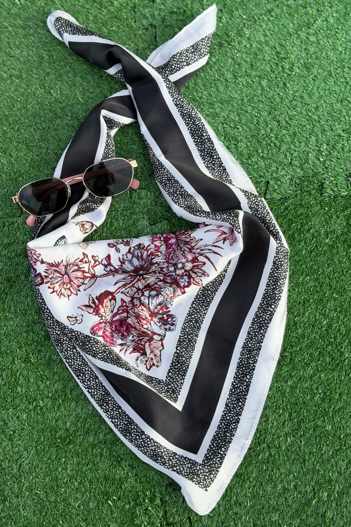 black scarf with red wild flowers resting on a turf backdrop.