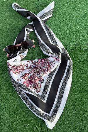 black scarf with red wild flowers resting on a turf backdrop.
