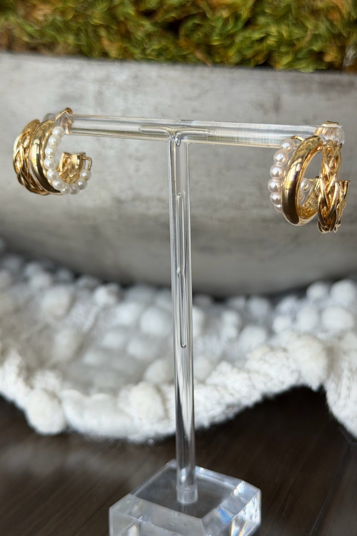 Gold hoop earrings on a clear stand with a blurred natural background