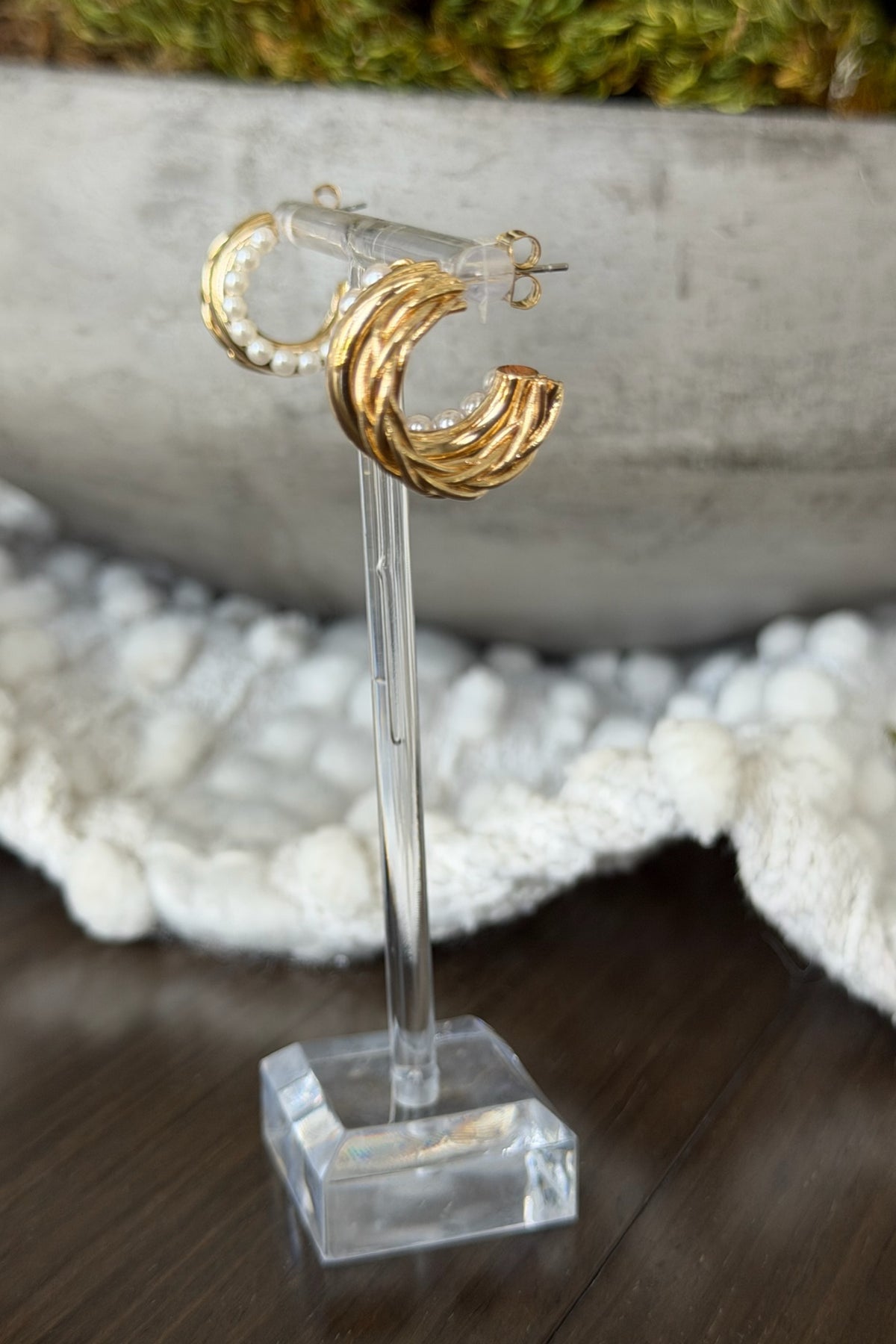 Gold hoop earrings on a clear stand with a blurred background