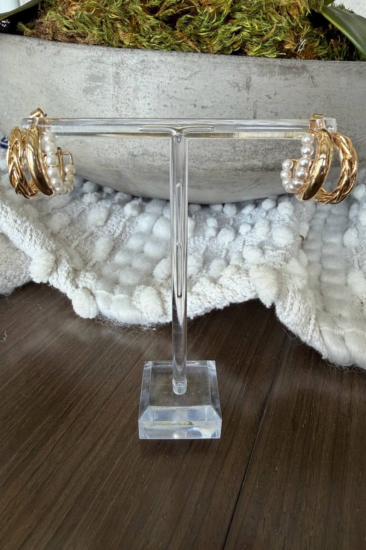 Gold hoop earrings on a clear T-shaped stand with a natural background
