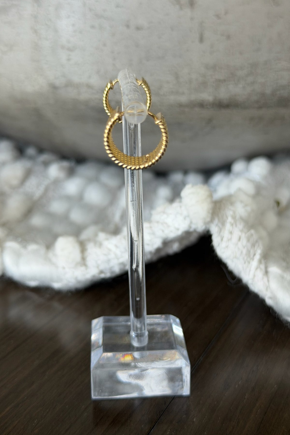 Gold hoop earring on a clear stand with a textured stone background