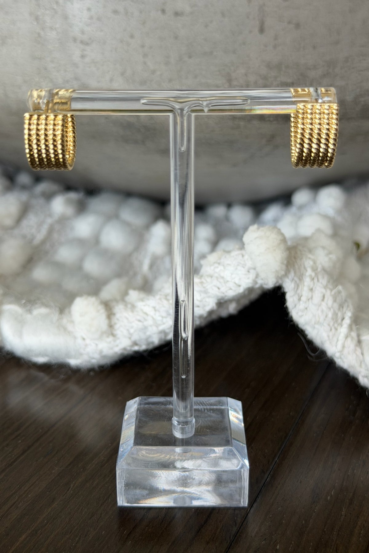 Gold hoop earrings on a clear T-shaped stand with a textured surface in the background.