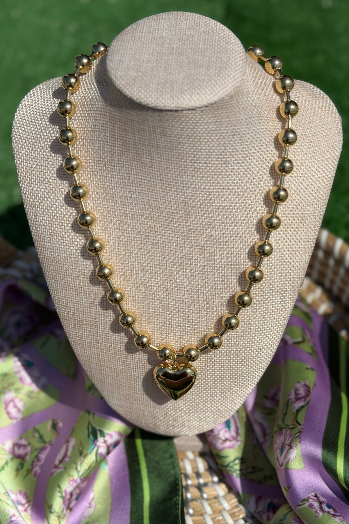 Necklace with a heart-shaped pendant on a beige mannequin bust against a floral fabric background