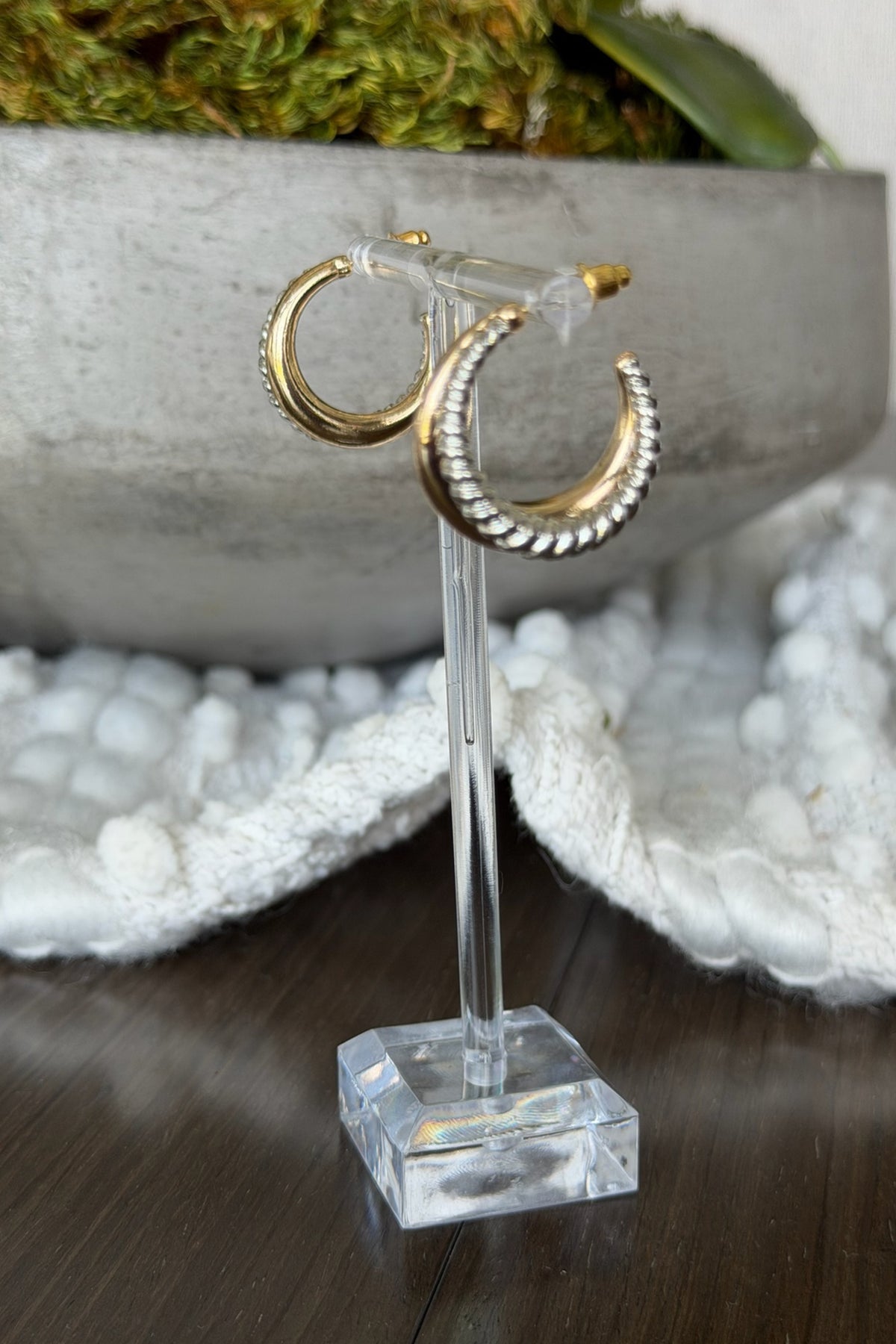 Gold hoop earrings on a clear stand with a blurred natural background