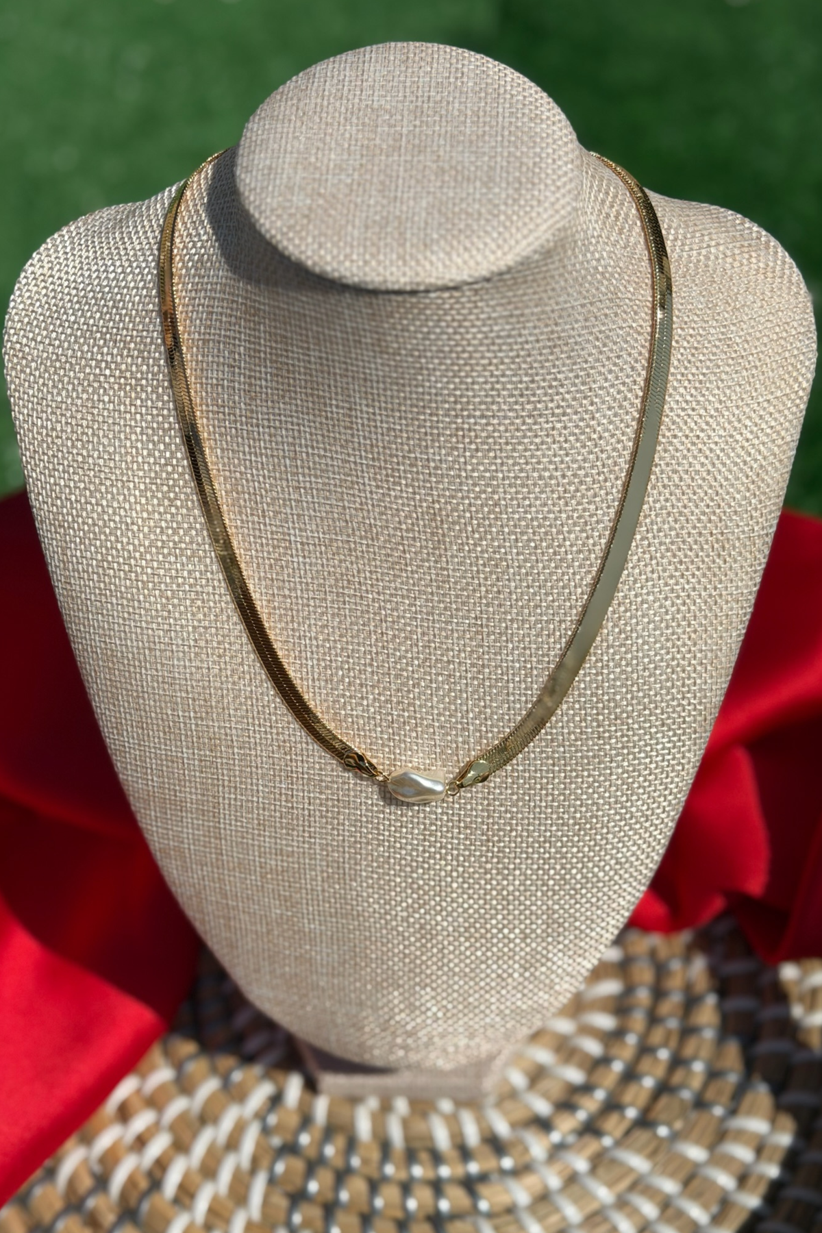 Gold necklace on a mannequin bust with a red fabric background