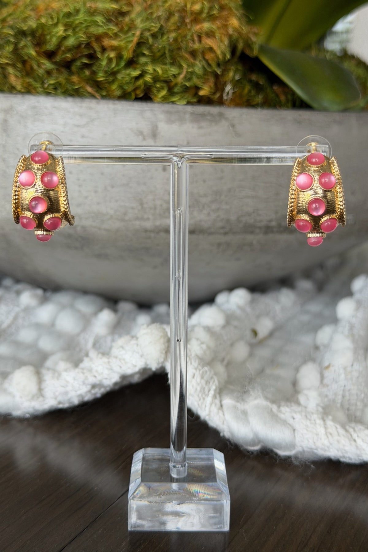 Gold and pink earrings on a clear stand with a natural background