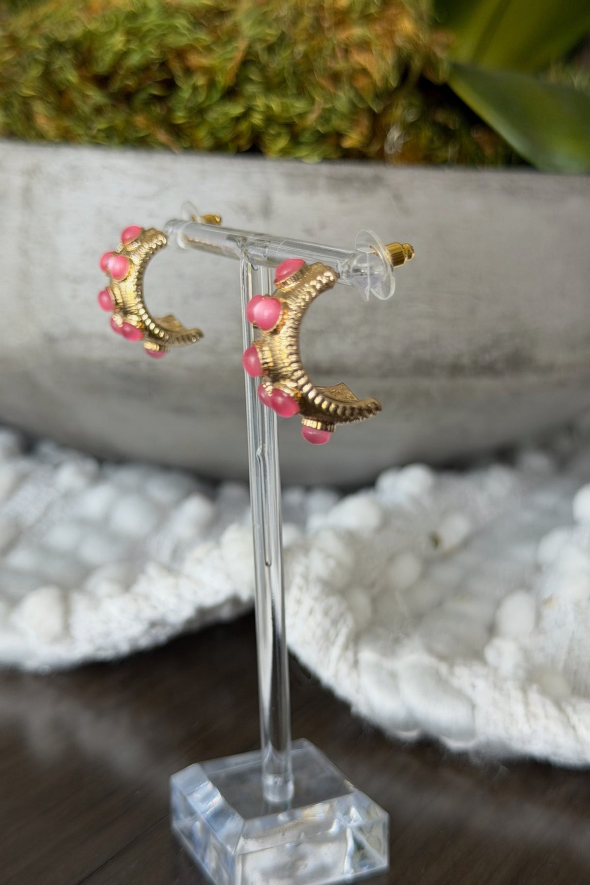 Gold earrings with pink beads on a clear stand against a natural background