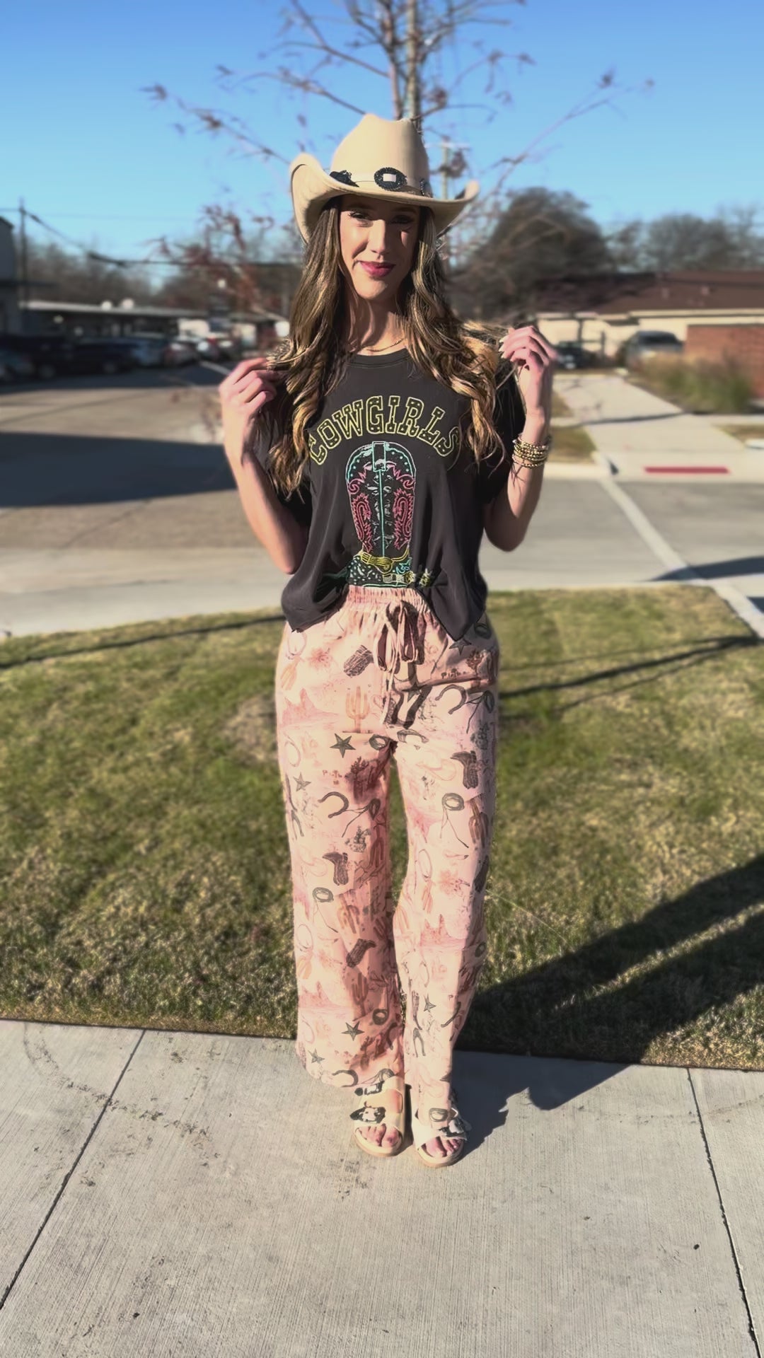 Woman wearing a graphic t-shirt and patterned pants with a wide-brimmed hat.