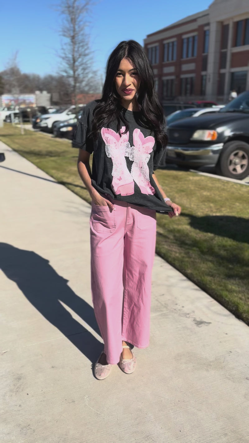 Woman wearing a black t-shirt with pink graphics and pink pants outside.