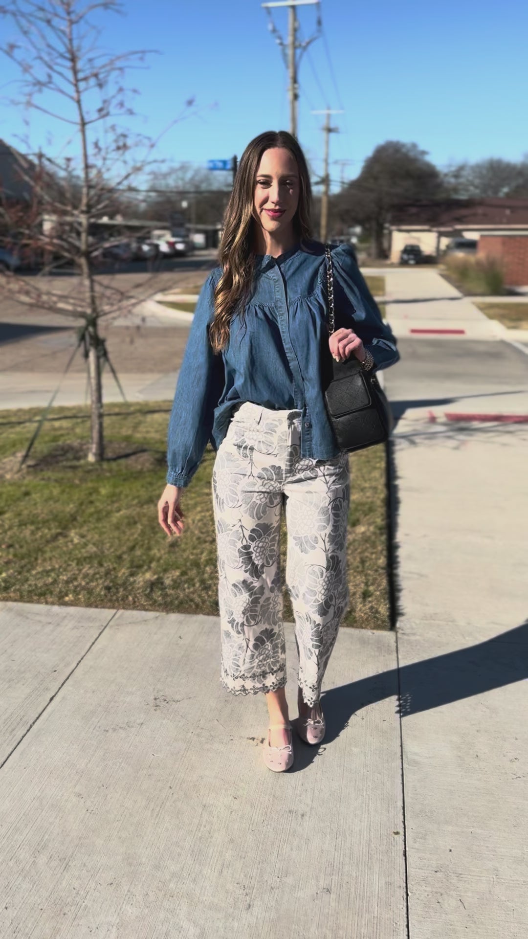Woman wearing a blue blouse and floral pants standing outside.