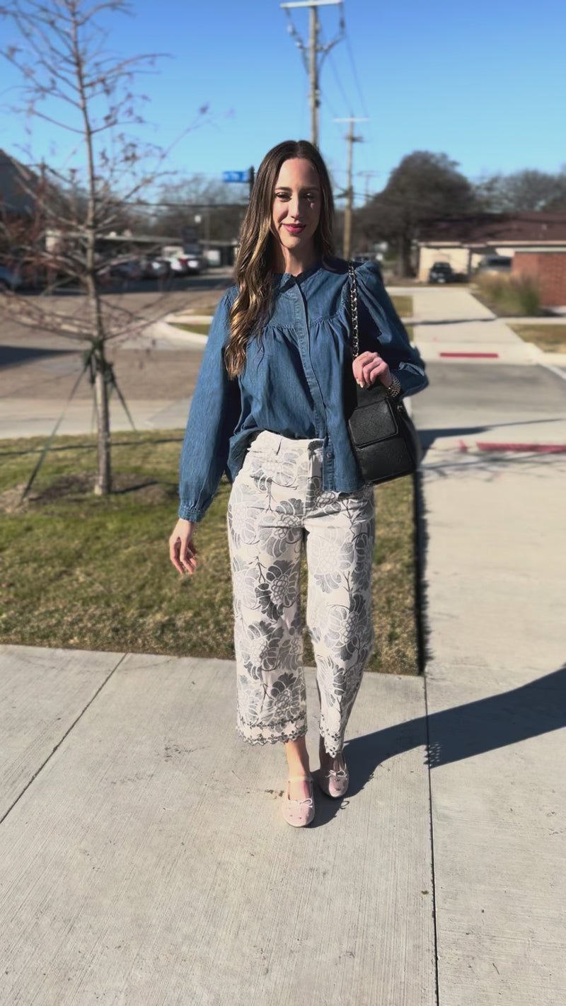 Woman wearing a blue blouse and floral pants standing outside.