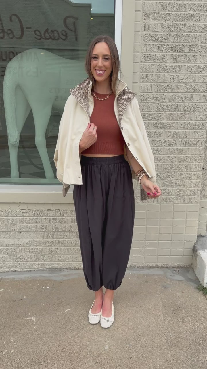Blonde model wearing an ivory multi jacket, cinnamon colored tank and black pants standing outside. Southern House Clothing