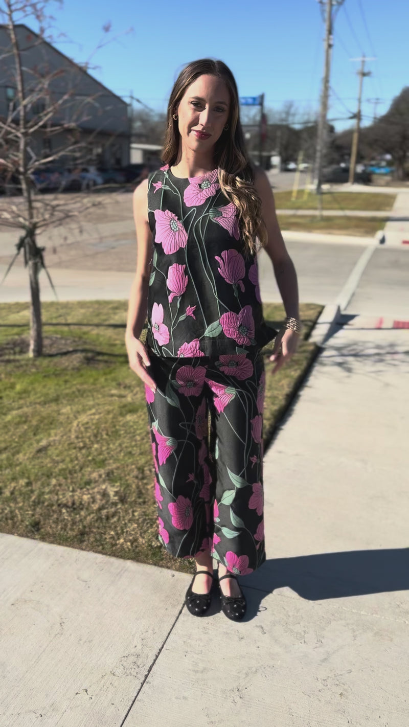 Person wearing a black jumpsuit with pink floral patterns on a concrete surface.