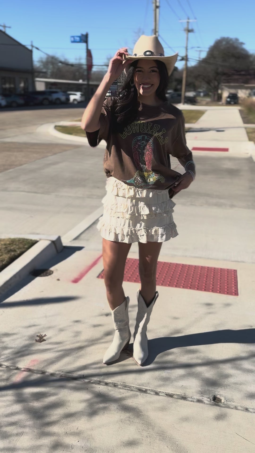 Woman wearing a brown 'Cowgirl' t-shirt and white skirt with a cowboy hat.