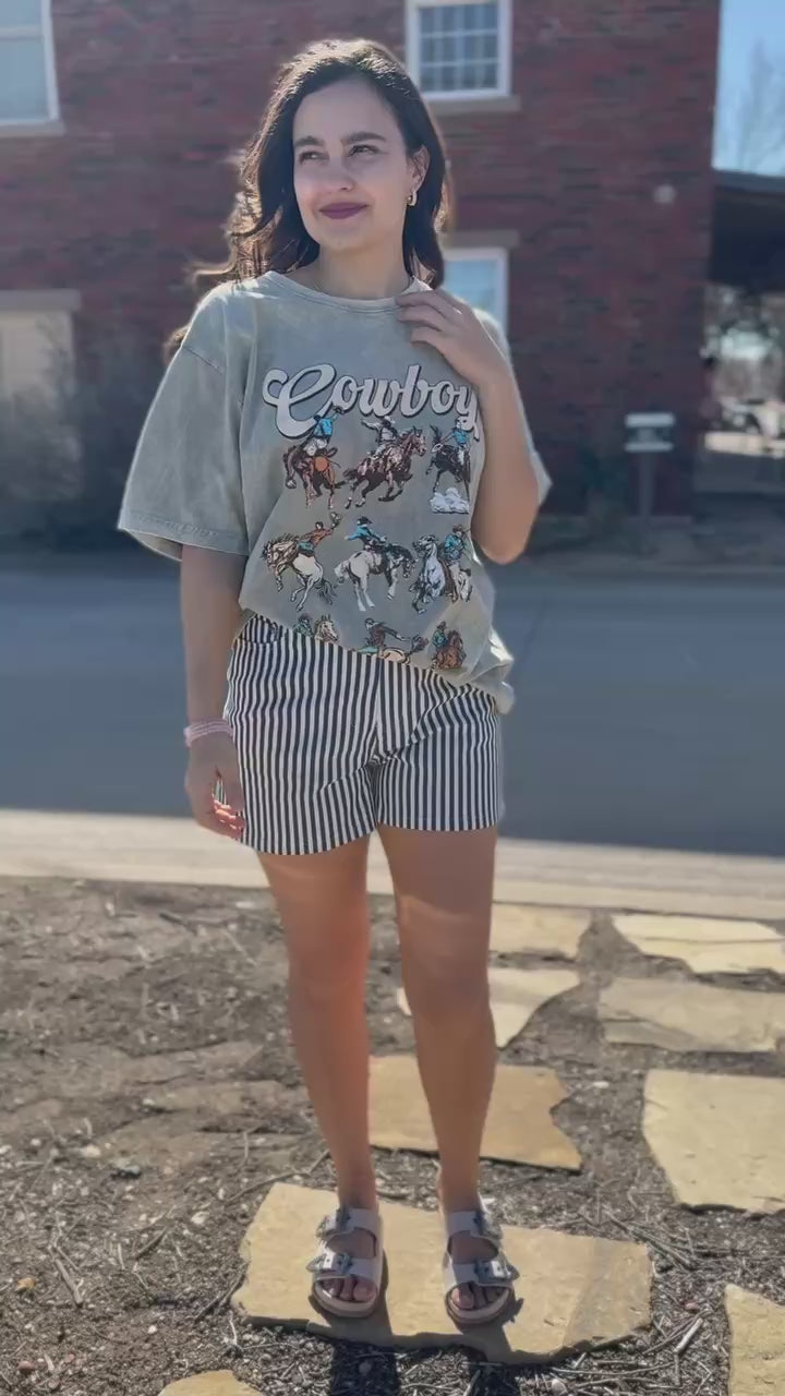 Woman wearing a graphic t-shirt and striped shorts standing in front of a brick wall.