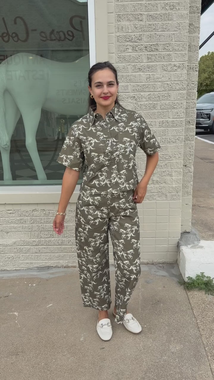Brunette model wearing an olive colored denim set with running horse detail and white slides standing outside. Southern House Clothing.