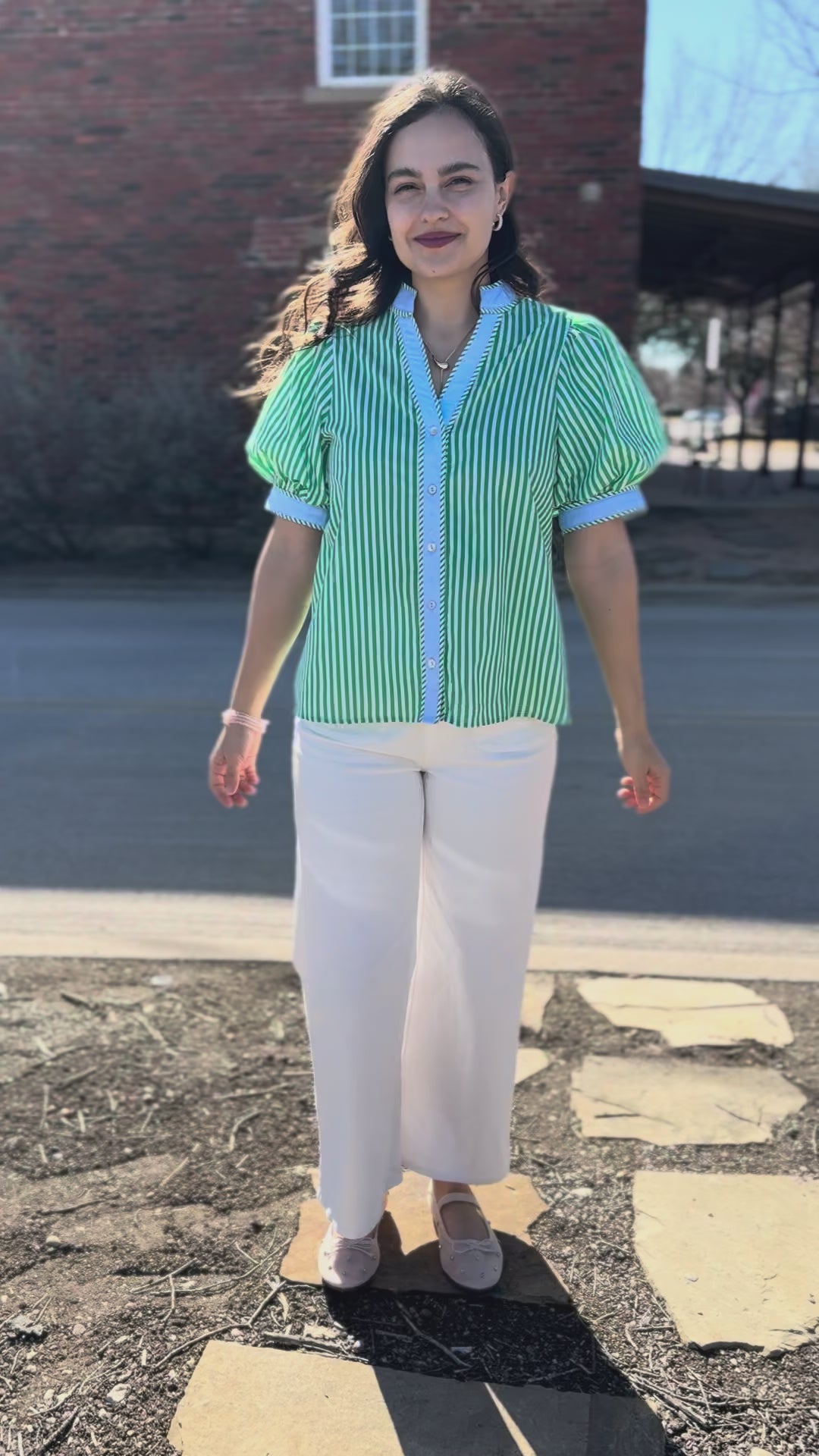 Woman wearing a green and white striped shirt with white pants on a city street.