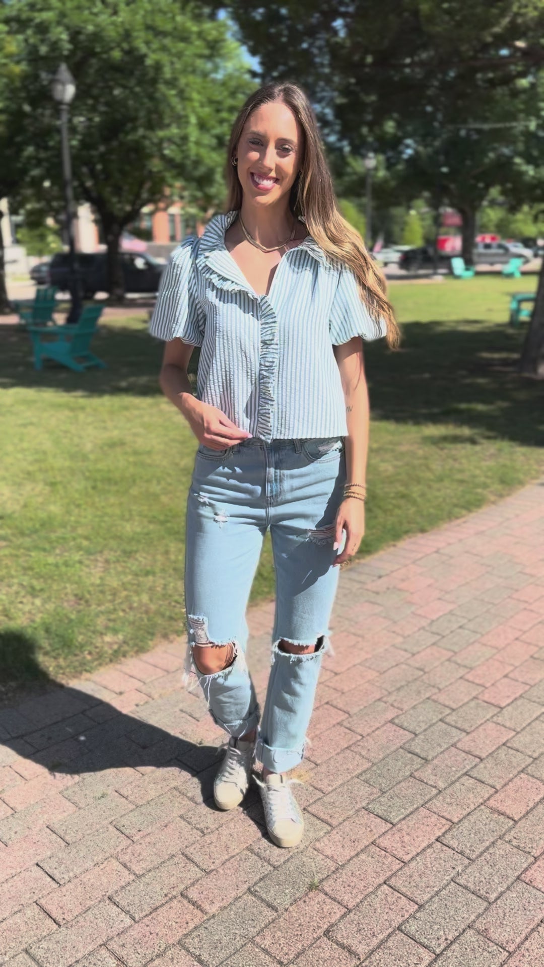 Woman wearing a light blue striped shirt and jeans standing outside.
