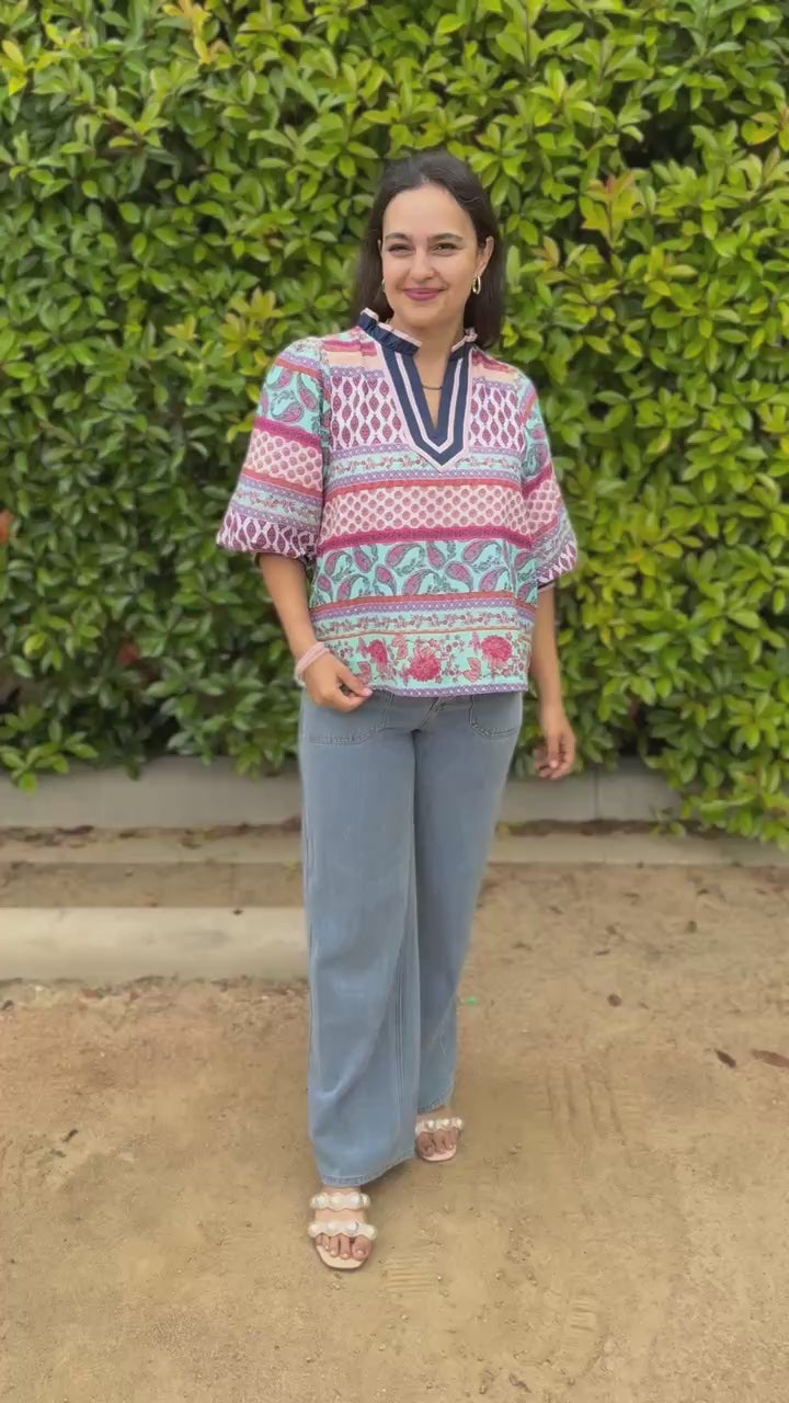 Woman wearing a colorful patterned blouse and jeans standing outdoors.