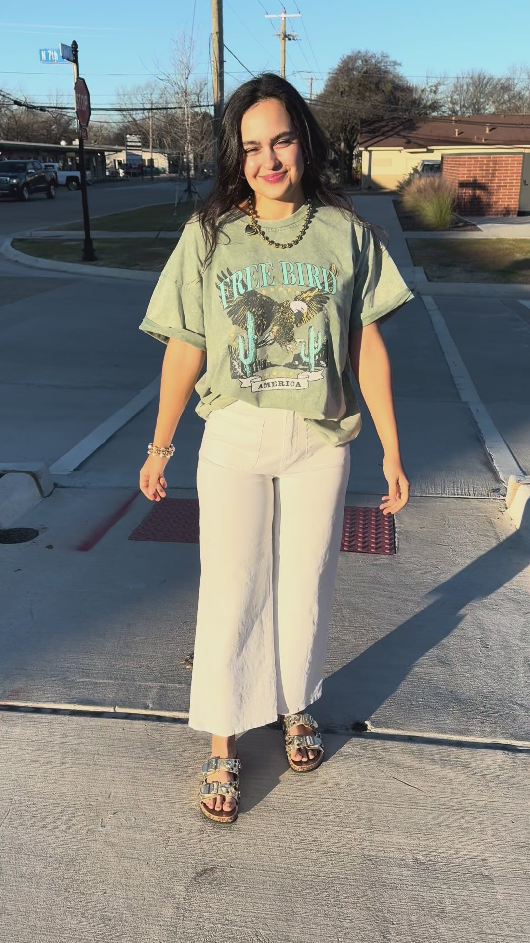 Woman wearing a green graphic t-shirt with an eagle design and text with white pants outside.