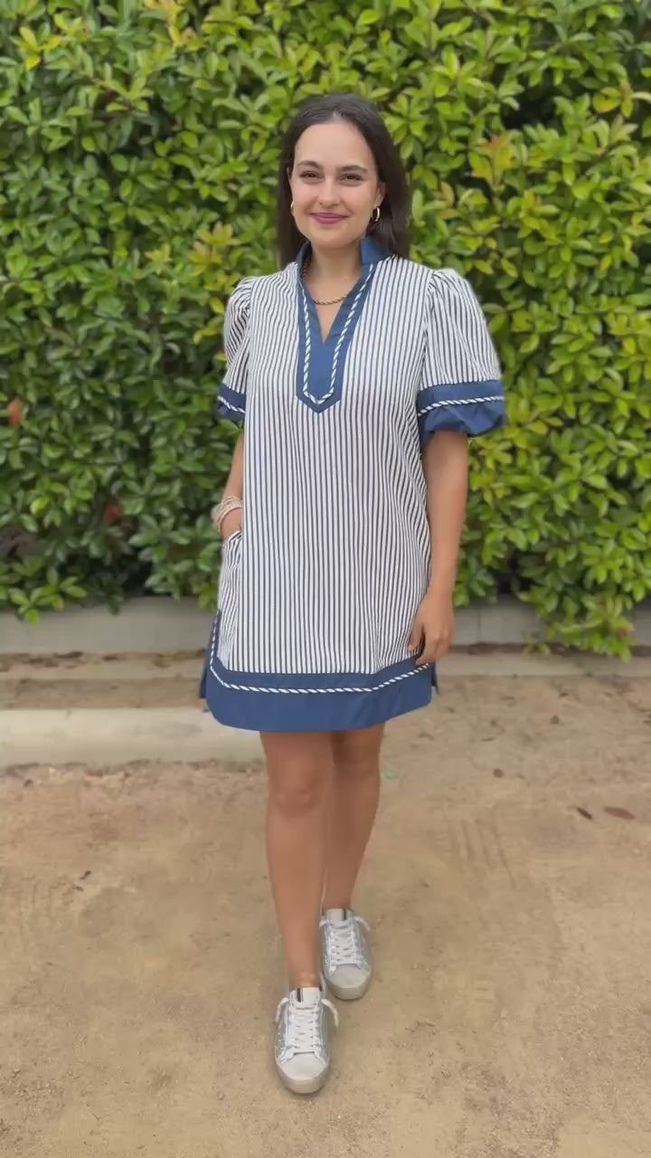 Woman in a blue and white striped dress standing in an outdoor setting with plants.