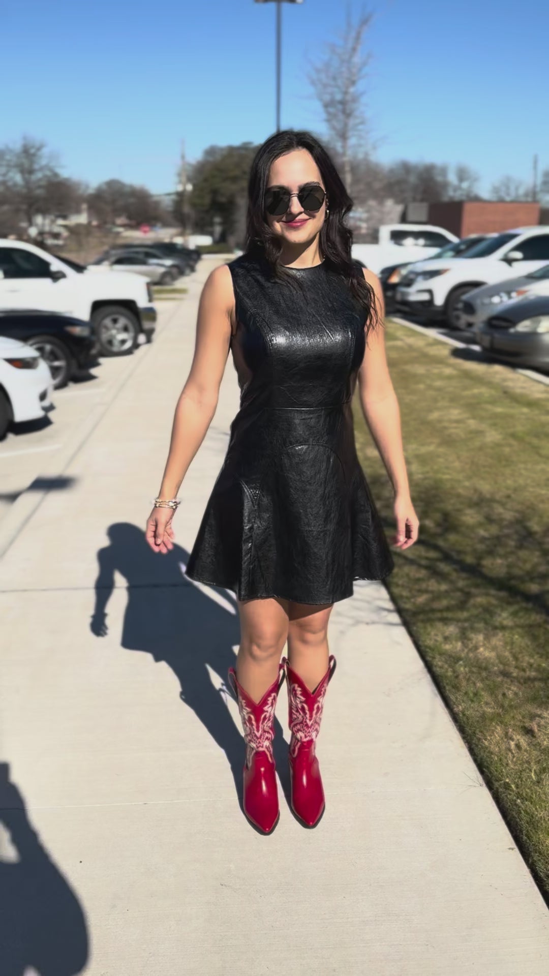 Woman wearing a black leather dress and red cowboy boots standing outside.