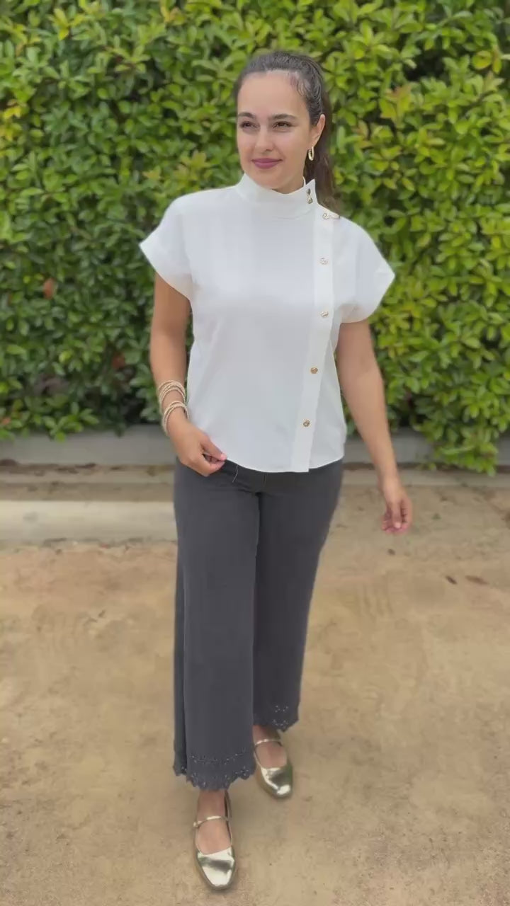 Woman wearing a white blouse with buttons and gray pants in an outdoor setting
