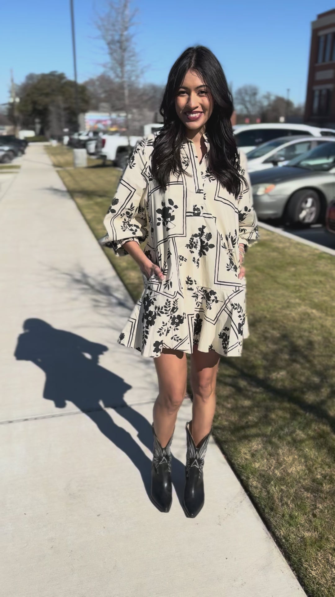 Woman in a floral dress and black boots walking outdoors.