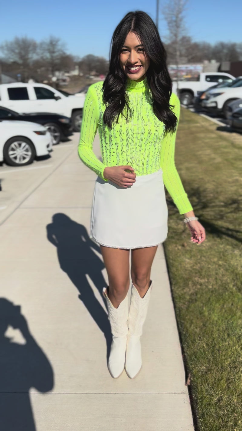 Woman wearing a bright green mesh top and white skirt outdoors.