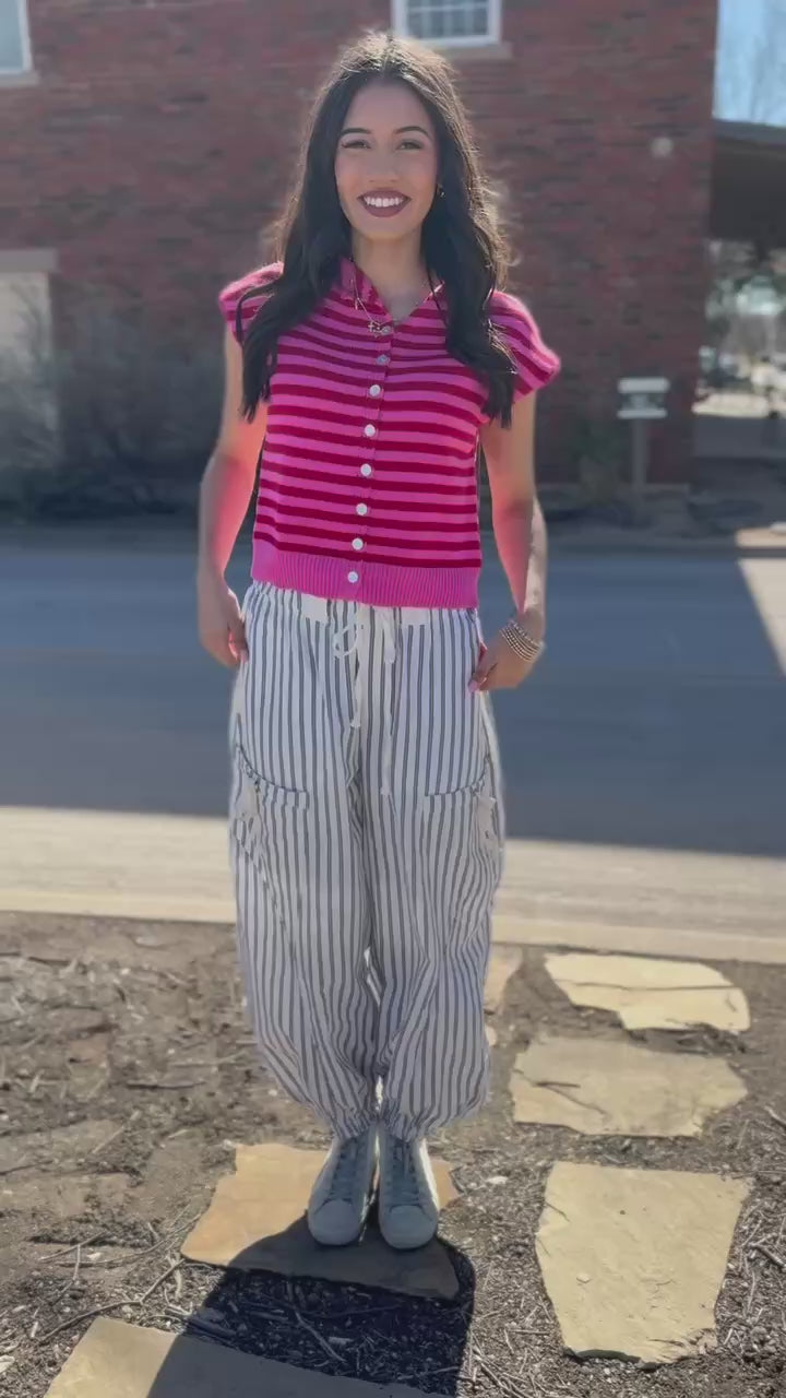 Person wearing a pink striped shirt and white pants on a street.