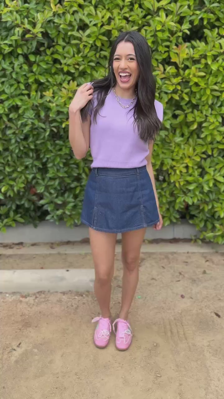 Woman wearing a purple sleeveless top and denim skirt outdoors.