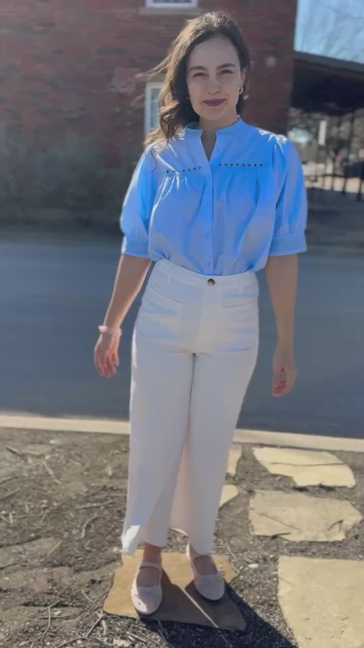 Woman wearing a light blue blouse and white pants outside.