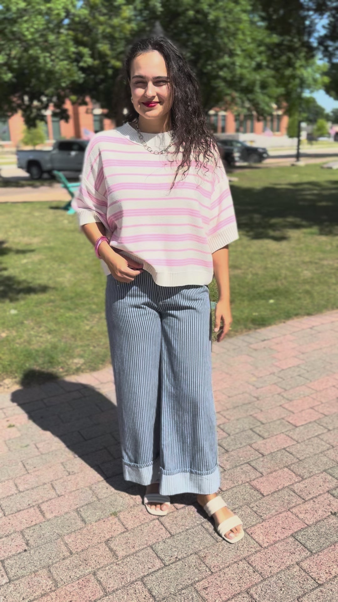 A woman wearing a pink and white striped knit sweater and blue-and-white striped pants, standing outside.