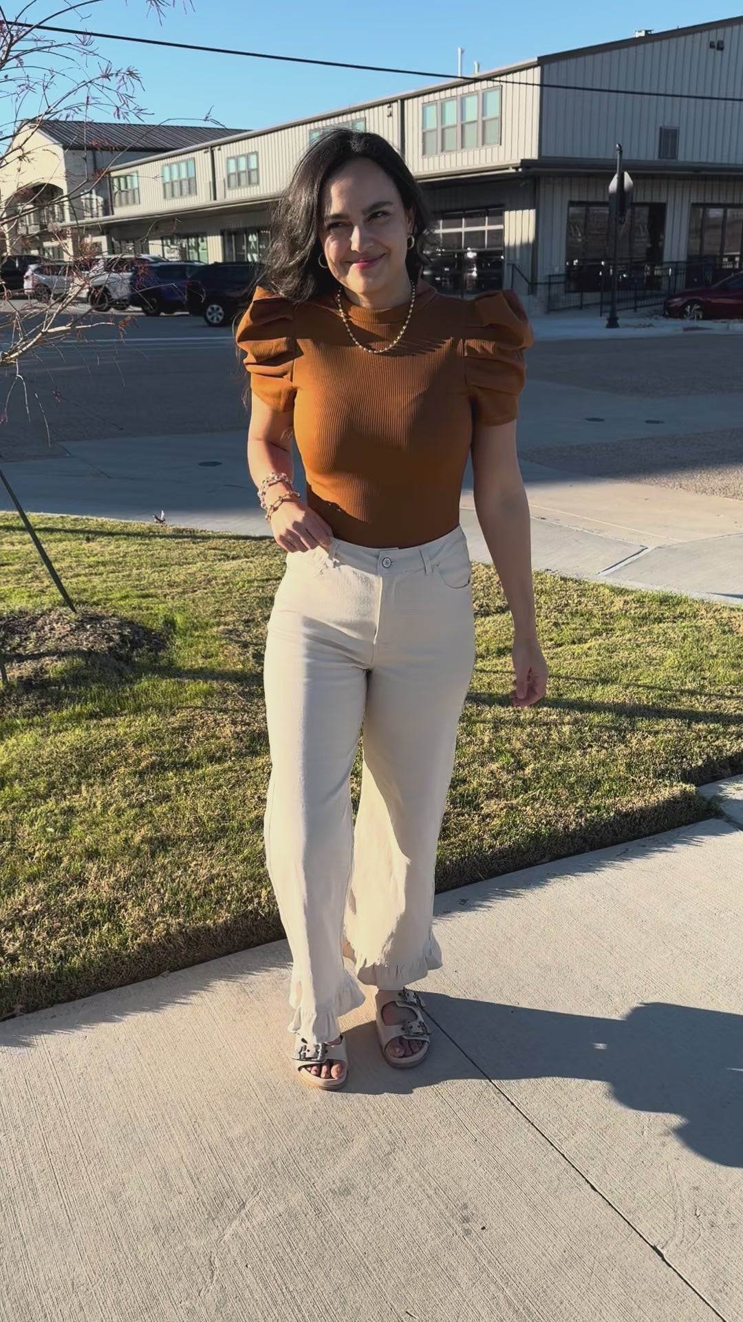 Woman wearing a brown top and white pants standing outdoors.