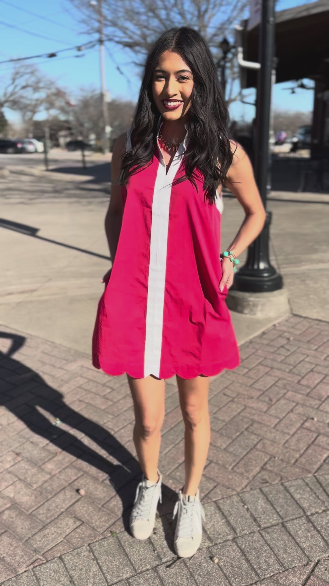 Woman wearing a red dress with a white stripe standing outdoors.