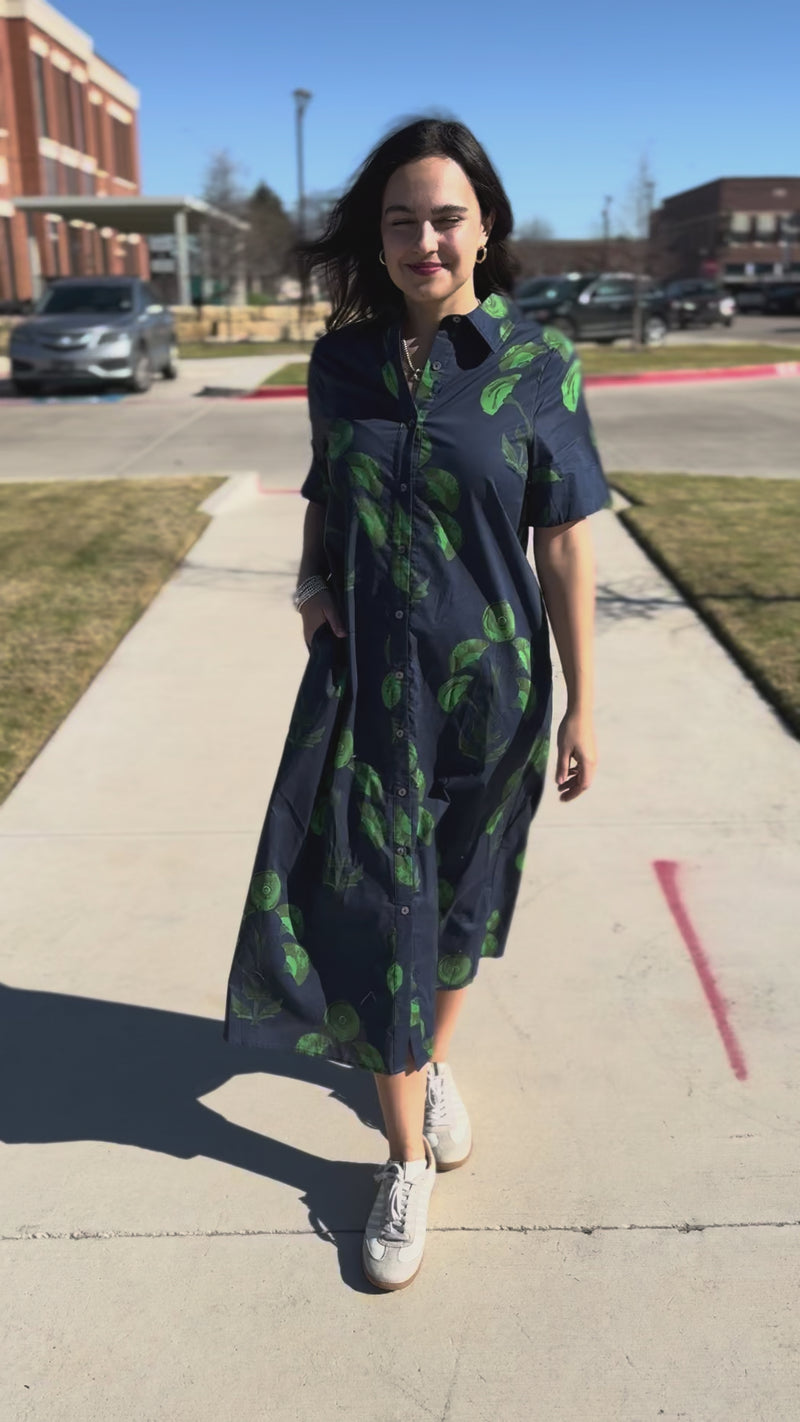 Woman wearing a long blue dress with green patterns outside.