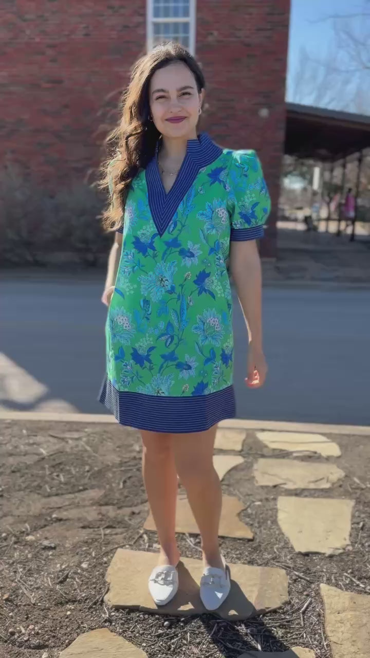 Woman wearing a green floral dress with purple accents standing on a sidewalk.