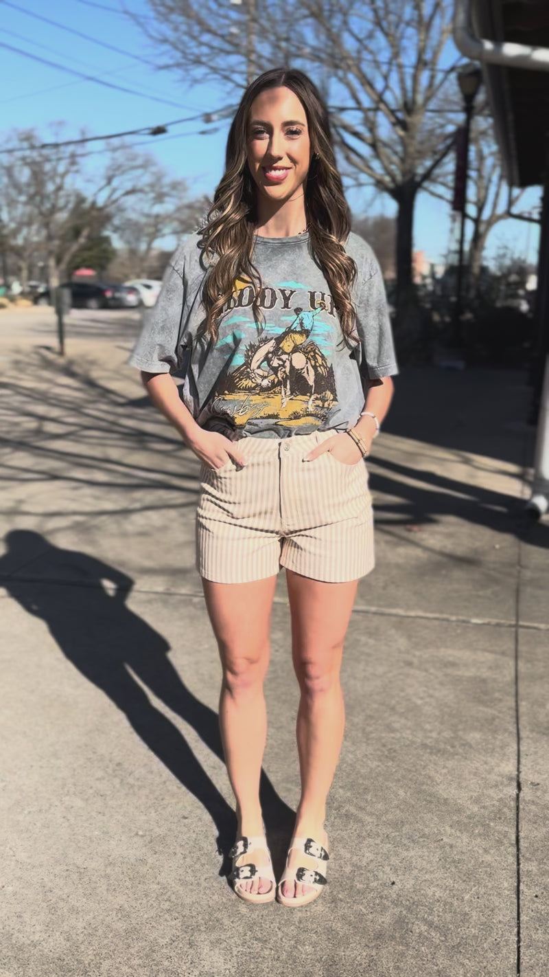 Woman wearing a graphic t-shirt and shorts standing in front of a door.