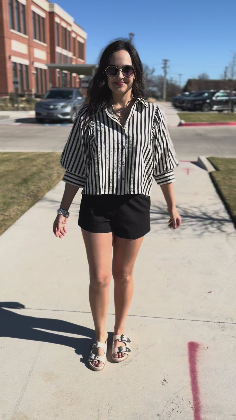 Woman wearing a black and white striped shirt and black shorts outside.