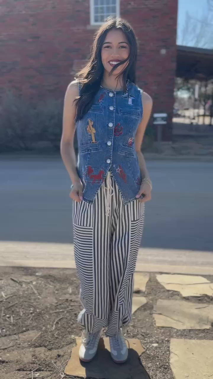 Woman wearing a denim vest over a striped pant on a city street.