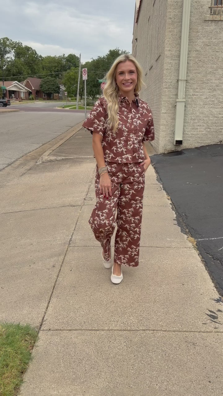 Blonde model wearing the Cibolo Running Horses Button-Up Top – Brown and matching denim bottoms - Cibolo Running Horses Wide Leg Pants – Brown standing outside. Southern House Clothing