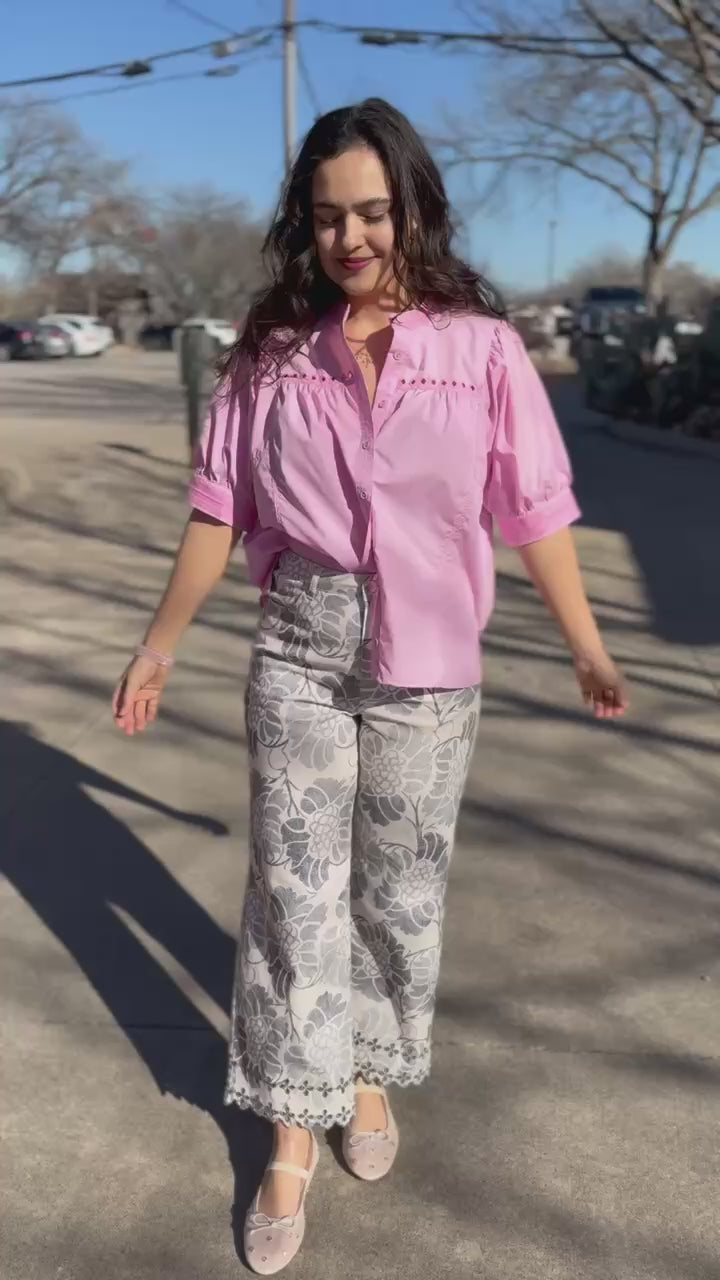 Woman wearing a pink blouse with white floral pants outside.