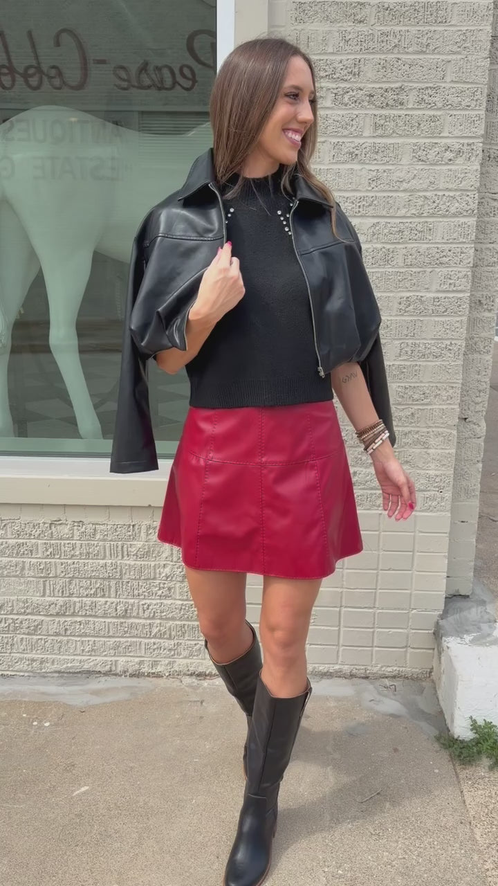 Blonde model standing outside wearing the Lennox Cropped jacket in black with the Harriett Black riding boots and a red skirt. Southern House Clothing