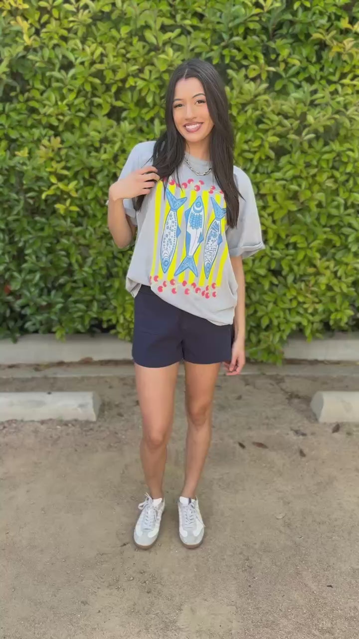 Woman wearing a gray t-shirt with a colorful design and navy shorts outdoors.