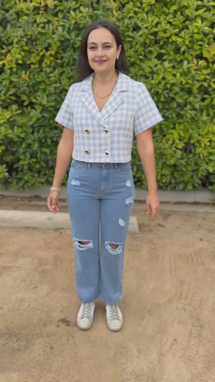 Woman wearing a light blue checkered blouse and ripped jeans outdoors.